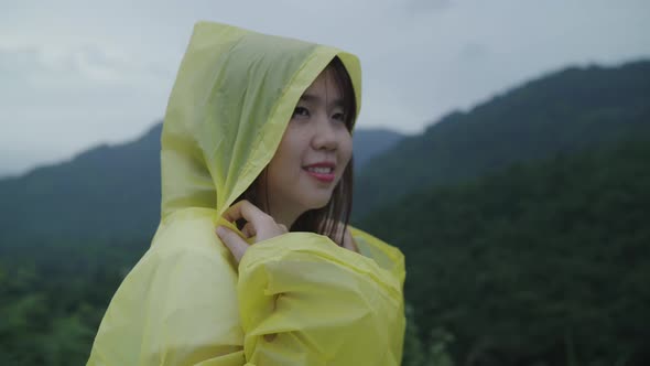 Young Asian woman feeling happy playing rain while wearing raincoat walking near forest.