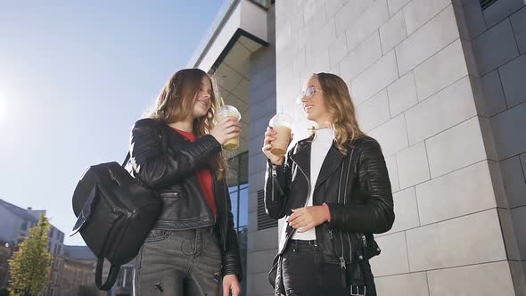 Two Teen Girls in Stylish Clothing clinking glasses and drinking fresh juice