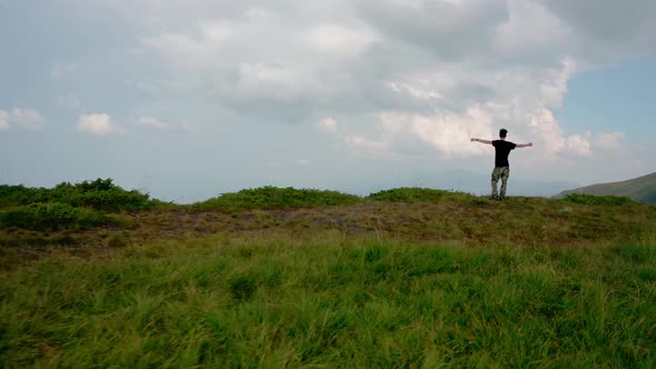 Aerial Drone View. Flying Around Young Man Standing on Top of the Mountain at Sunset 