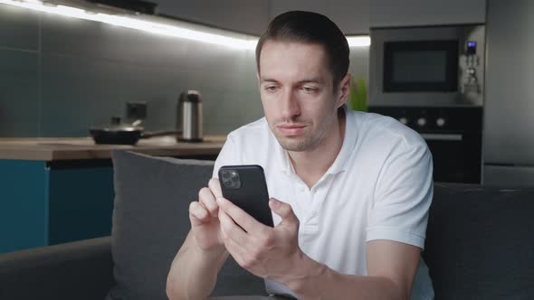 Young Man Using Smartphone App While Sitting on Sofa at Home at Night