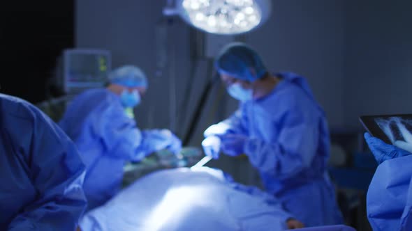 Surgeons wearing face masks operating and looking at x ray on tablet in operating theatre