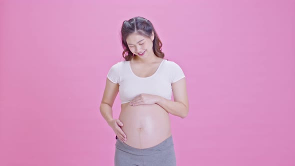 Happy Pregnant Woman standing smile and stroking big belly with love isolated on pink