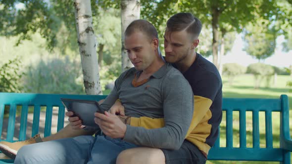 Gay Couple with Digital Tablet Relaxing on Bench