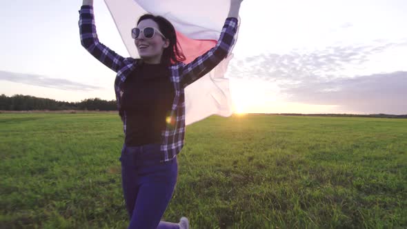 Young Positive Woman in a Shirt Runs Across the Field at Sunset with the Flag of Japan