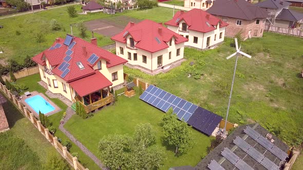 Aerial View of a Residential Private House with Solar Panels on Roof and Wind Generator Turbine