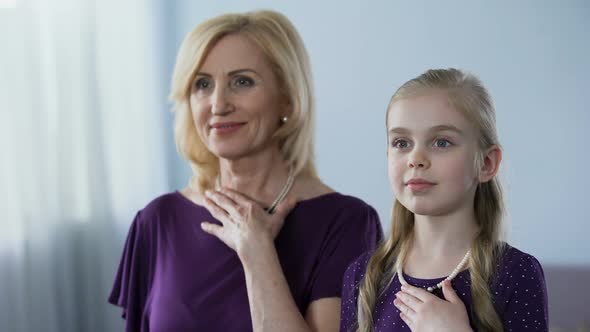 Blond Grandmother and Granddaughter With Pearl Necklaces Looking in Mirror