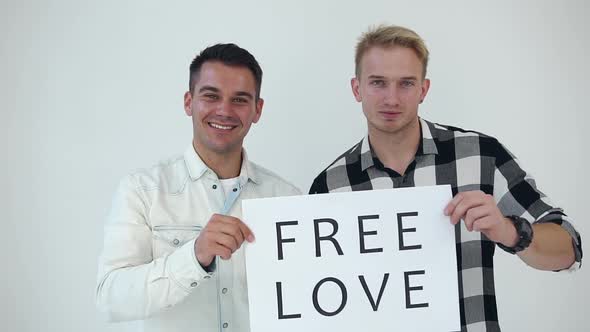 Smiling Two Men which Posing on Camera with Poster "Free Love" on the White Background