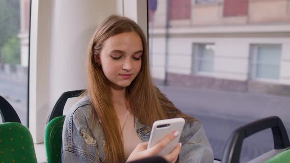 Young Girl Using Mobile Phone Internet Social Network Application While Traveling By Bus in City