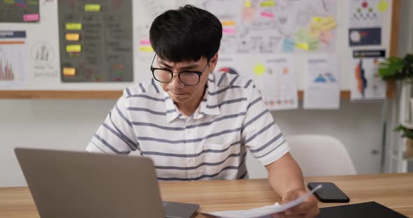 Asian man glasses typing laptop and checking document