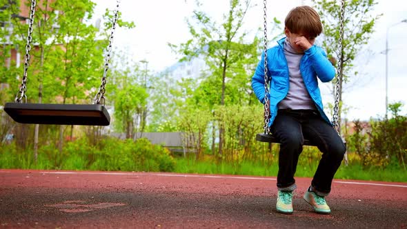 A Little Sad Lonely Boy Sitting on the Swings on the Playground