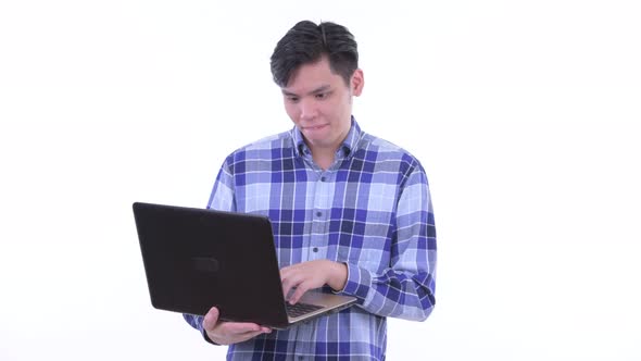 Happy Young Asian Hipster Man Thinking While Using Laptop