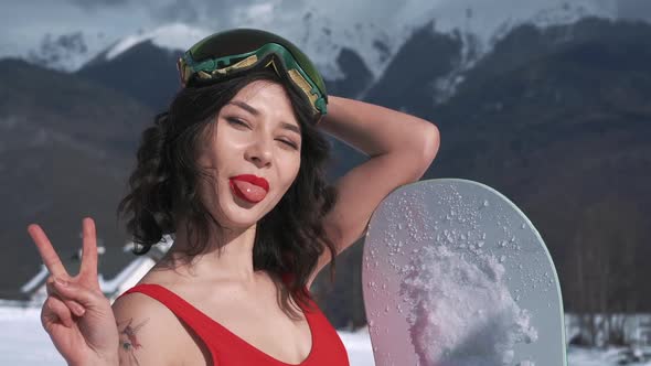 Portrait of Young Mixed Race Woman in Snowboard Goggles and Swimsuit at Winter Ski Resort at Snowy