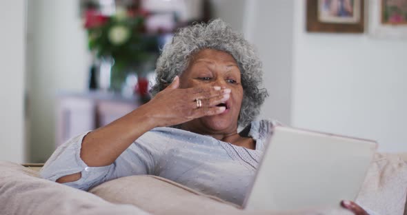 Senior african american woman waving and blowing kisses while having a video call on digital tablet