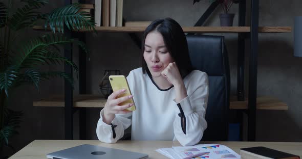 Smiling Relaxed Asian Millennial Woman Hold Smartphone Watching Social Media Stories Video Sit on
