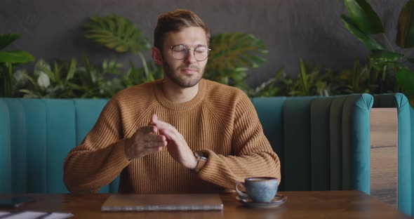 Front View of Handsome Man in Eyeglasses in Brown Sweater Finishes Work at Laptop Close It and