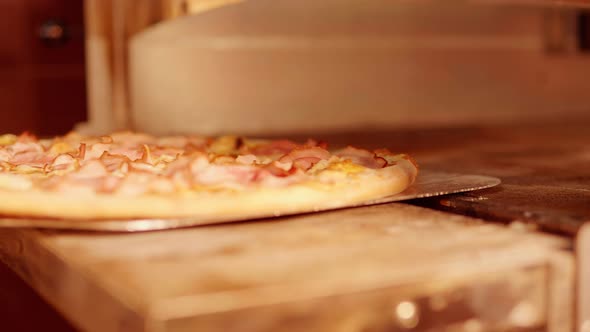 The pizza maker takes out the finished pizza from the oven