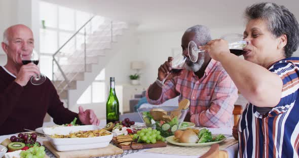 Diverse senior couples sitting by a table drinking wine and eating dinner