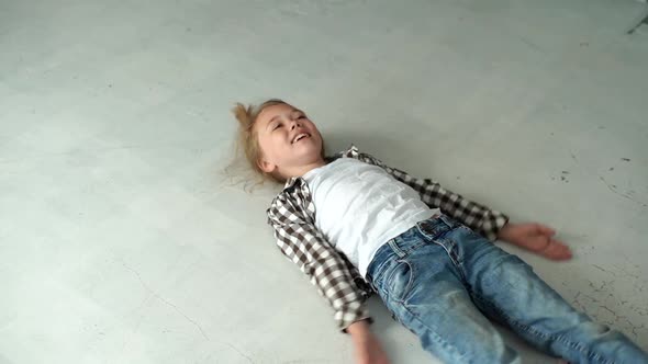 Highangle View of Happy Laughing Little Girl Lying on Floor Spreading Arms and Legs Making Angel