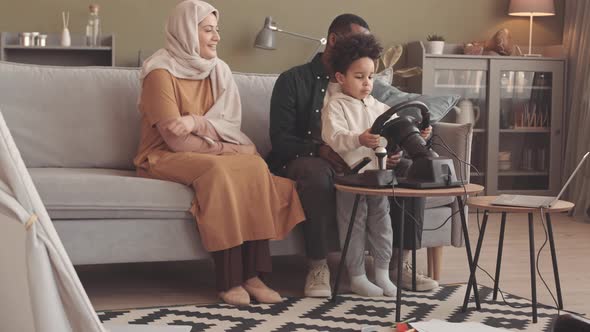 Little Boy Playing Race Video Game with Steering Wheel at Home