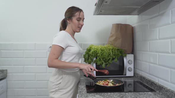 Happy Girl Is Singing While Cooking Vegetable Meal In The Kitchen