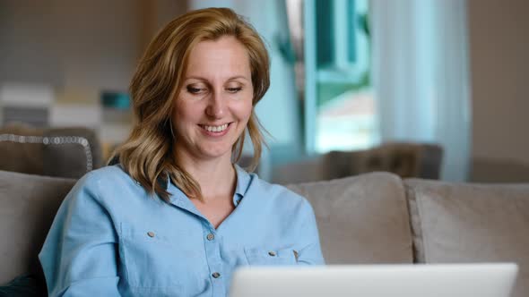 Smiling Middle Age Woman Using Laptop Sitting on Sofa and Having Video Call Rbbro