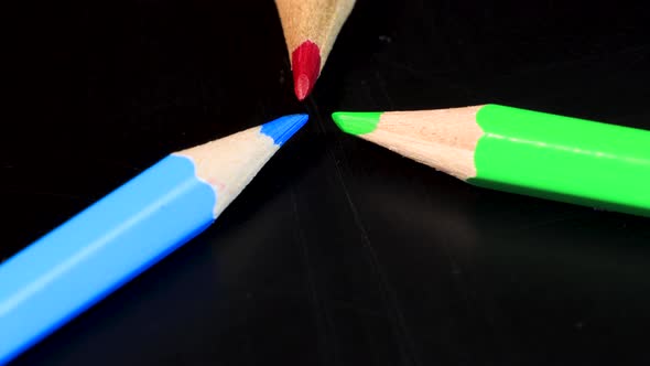 Red, green and blue crayons pointing at each other and slowly rotating in 4k, macro shot. Light prim