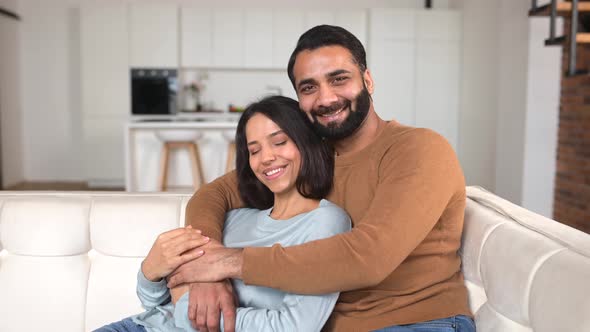 Closeup of Happy Interracial Couple Looking at the Camera While Sitting at the Sofa