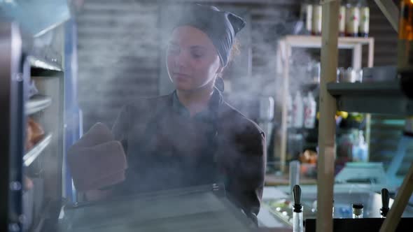 Small Business, Female Baker in Gloves and Uniform Takes Out Freshly Baked Bun From Hot Oven, Pastry