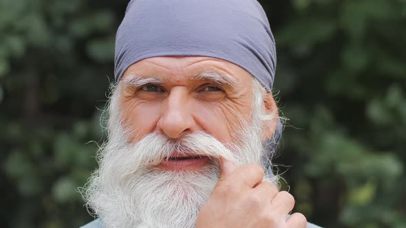 Close Up Portrait of Happy Senior Happy Man with Huge Gray Beard Straightens Mustache Looking