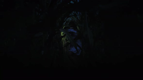 Frightened Young Woman with Flashlight Runs Through the Thicket at Night