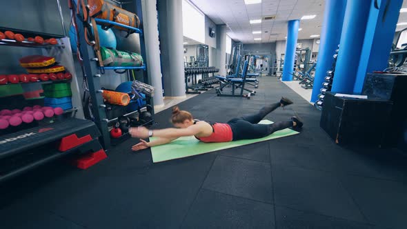 Female athlete in sportswear training indoors. Young woman lying on a mat and lifting arms