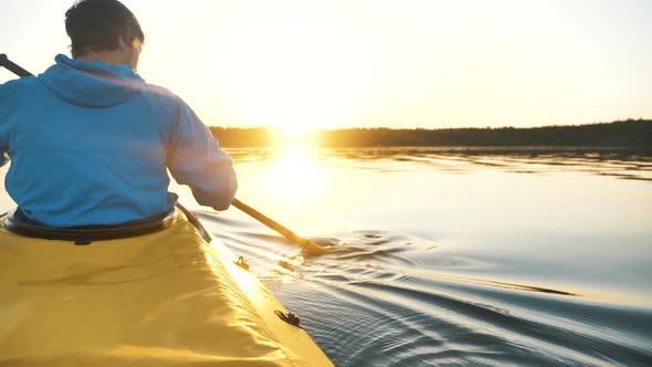 Young Man in Blue Jacket Paddles a Kayak on Lake at Sunset, Outdoor Activities Close-up