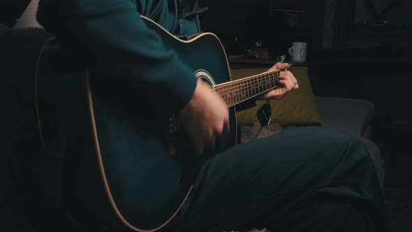 Man Plays a Pick on a Modern Guitar in the Dark