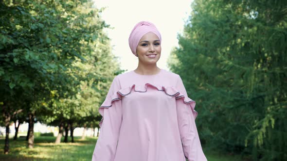Young Muslim Woman in a Turban Scarf Walks Through the Park Among the Trees