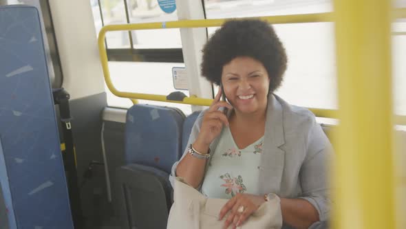 Happy plus size biracial woman talking on smartphone in bus