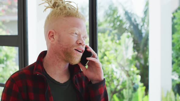 Albino african american man with dreadlocks using smartphone and looking at the window