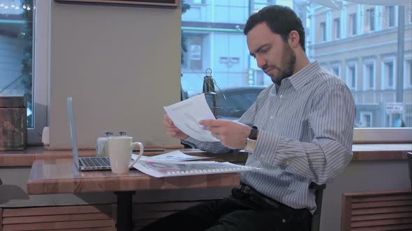 Exhausted Businessman in a Coffee Shop Searching in Documents