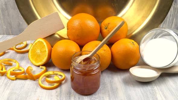 Oranges, sugar, a jar of jam and a copper bowl for making jam are on the kitchen table.