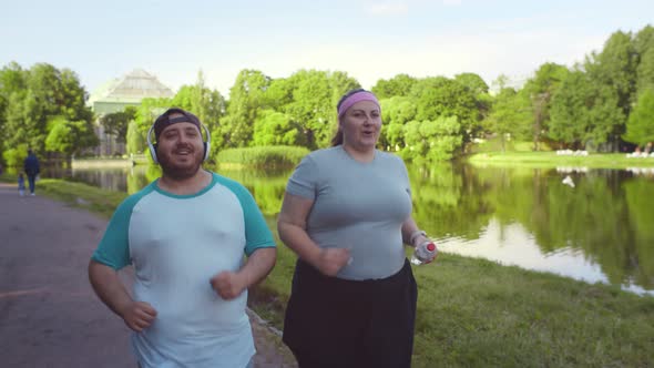 Overweight Young Couple Running Together in Summer Park