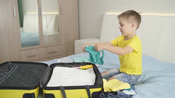 A Charming Boy Puts Things in a Yellow Suitcase for a Trip To the Sea on Vacation. The Concept of