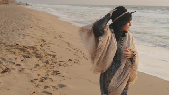 Portrait of Romantic Brunette Woman in Hat and Plaid Walking on the Beach in Autumn at Sunset or