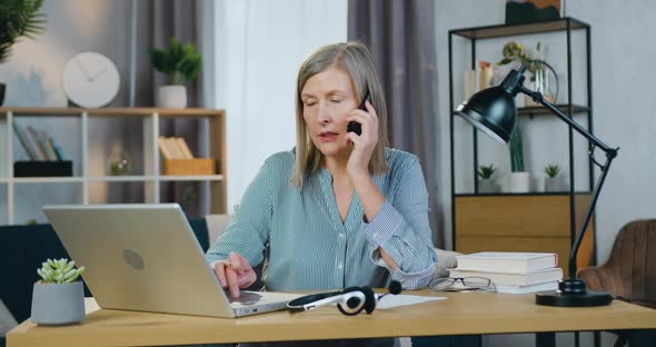 Senior Business Woman Talking on Mobile and Typing on Laptop