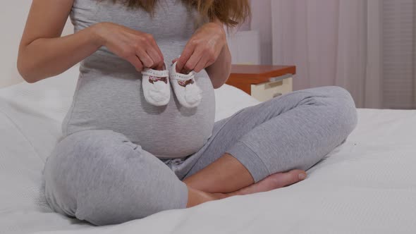 Pregnant Happy Woman Holding Baby Shoes in Her Hands. Mom Expecting Her Baby. Pregnant Woman Belly