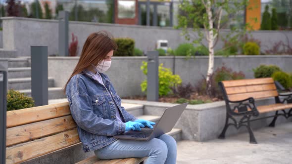 Girl in Gloves and Medical Mask Uses Laptop Outside