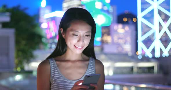 Woman Looking at Mobile Phone in City at Night 