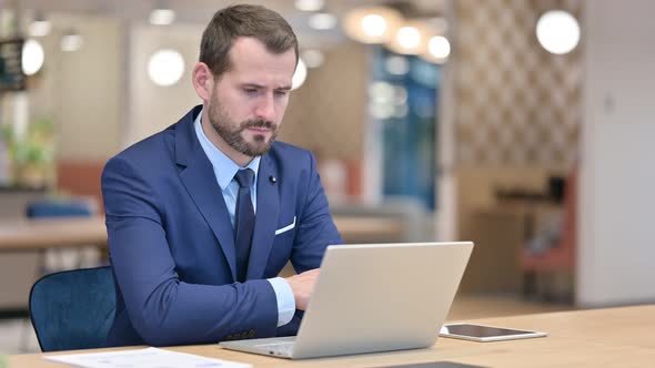 Pensive Businessman Thinking and Working on Laptop in Office 