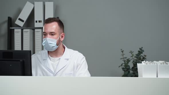 Man Doctor Wearing Protective Face Mask and Medical Gown Working on Computer Giving Delivery Box to