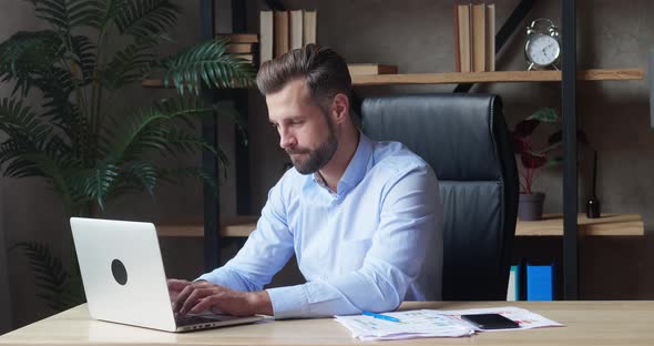 Happy Young Businessman in Blue Shirt Looking in Laptop Typing Text Enjoying Work Break Smiling