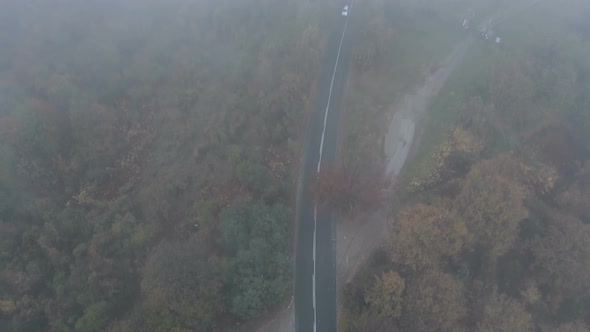 Drone Following White Car Speeding on Dark and Misty Mountain Road