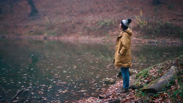 A Woman Stands on the Shore of a Forest Lake and Enjoys the View